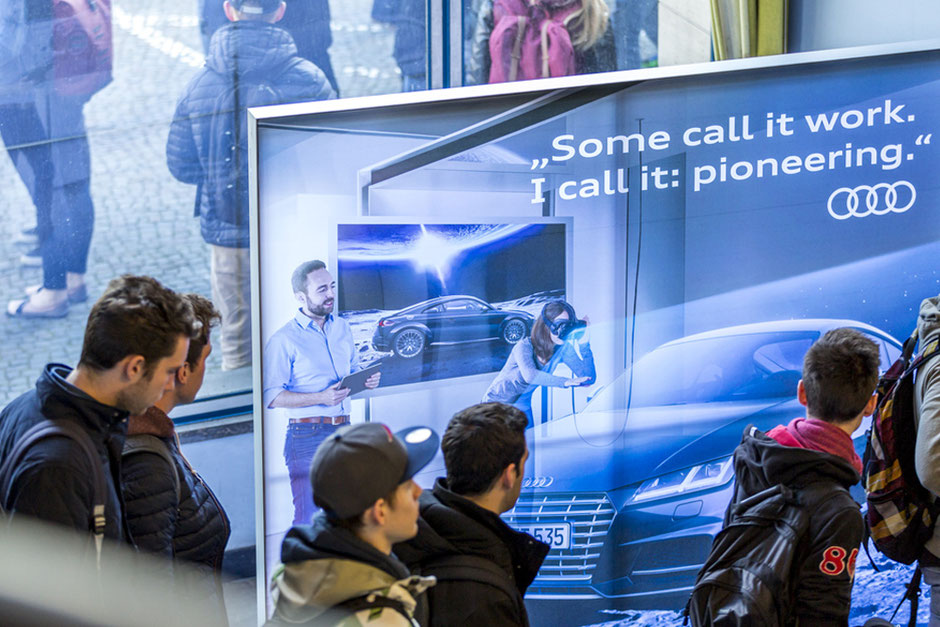 Eine Gruppe von Leuten, die vor einem Autowerbeplakat von Audi stehen