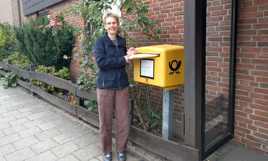 Delmenhorster Schriftstellerin Katy Buchholz steht am Briefkasten und schickt ein Buch im die Welt