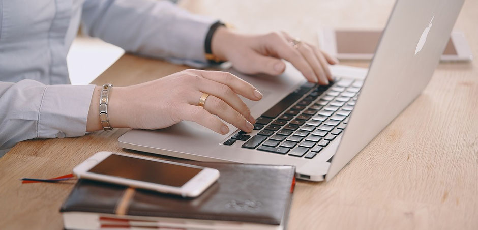 Frauenhände buchen am Laptop die Seminar-Versicherung der ERGO Reiseversicherung oder der Hanse Merkur oder der TravelSecure, ein Handy liegt auf dem Tisch. 