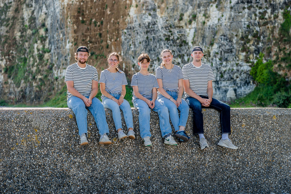 Cousins assis sur un muret sur la plage de Saint-Valery-en-Caux, avec les falaises en arrière-plan lors d’une séance photo familiale