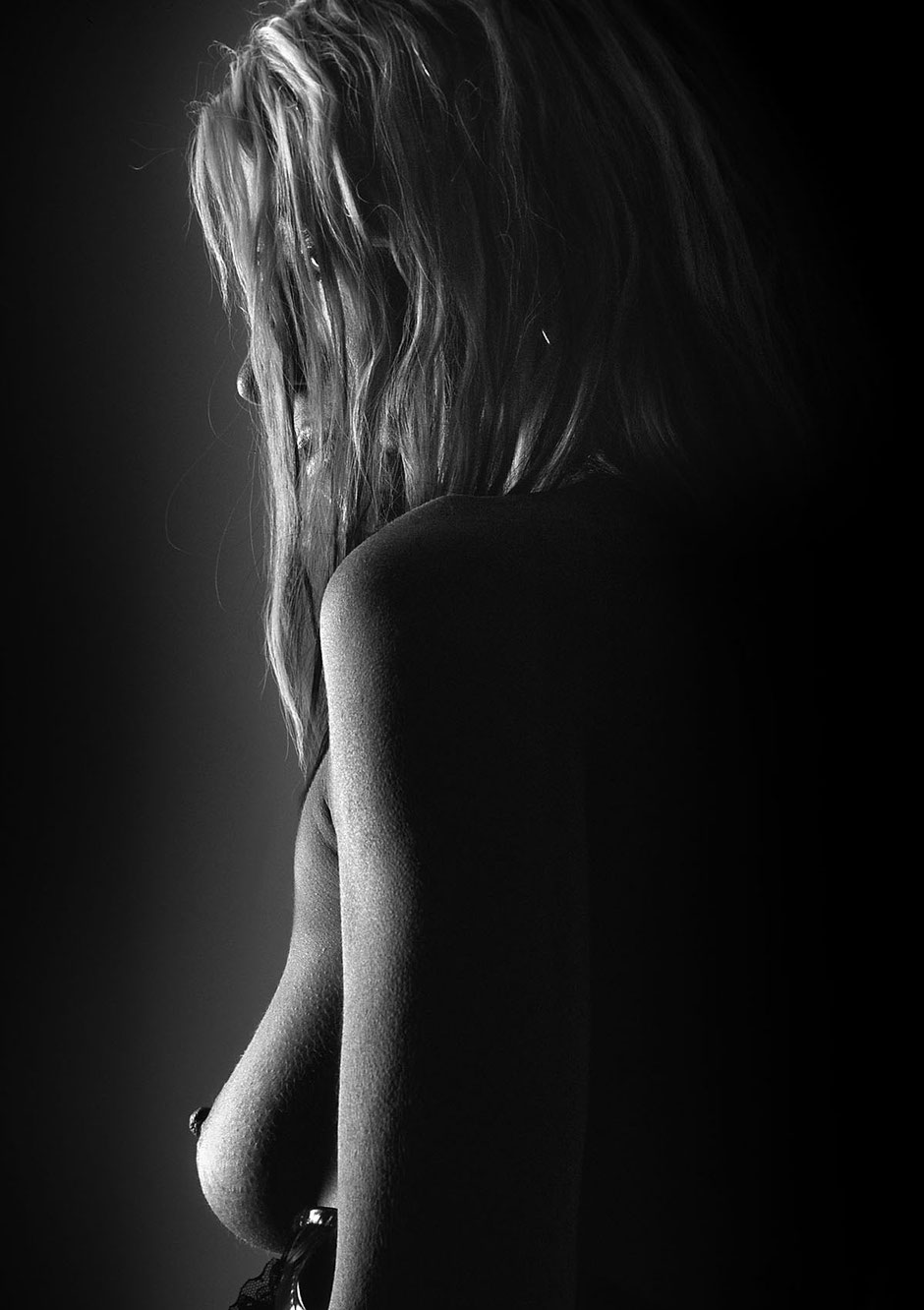 Black and white image with dramatic light of a nude woman with long hair well shaped breasts