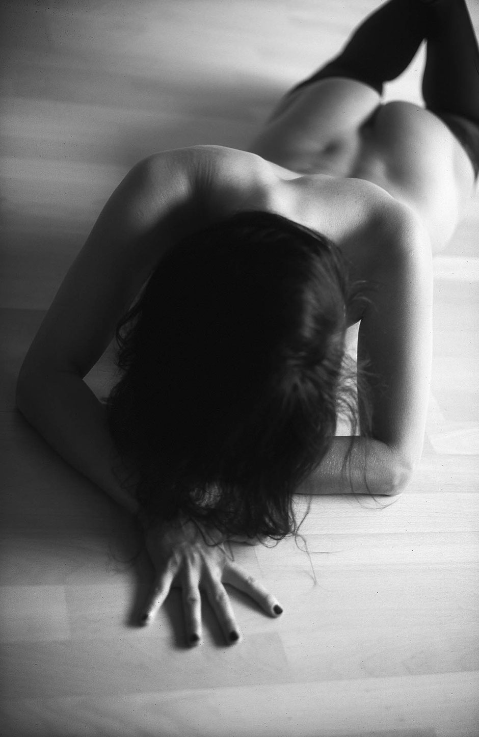 Black and white image of a nude athletic woman from above posing on the floor