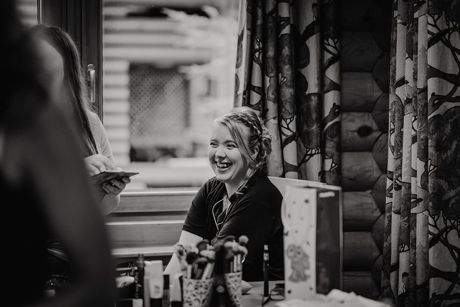 black and white photograph of a bride laughing as she has her make up done