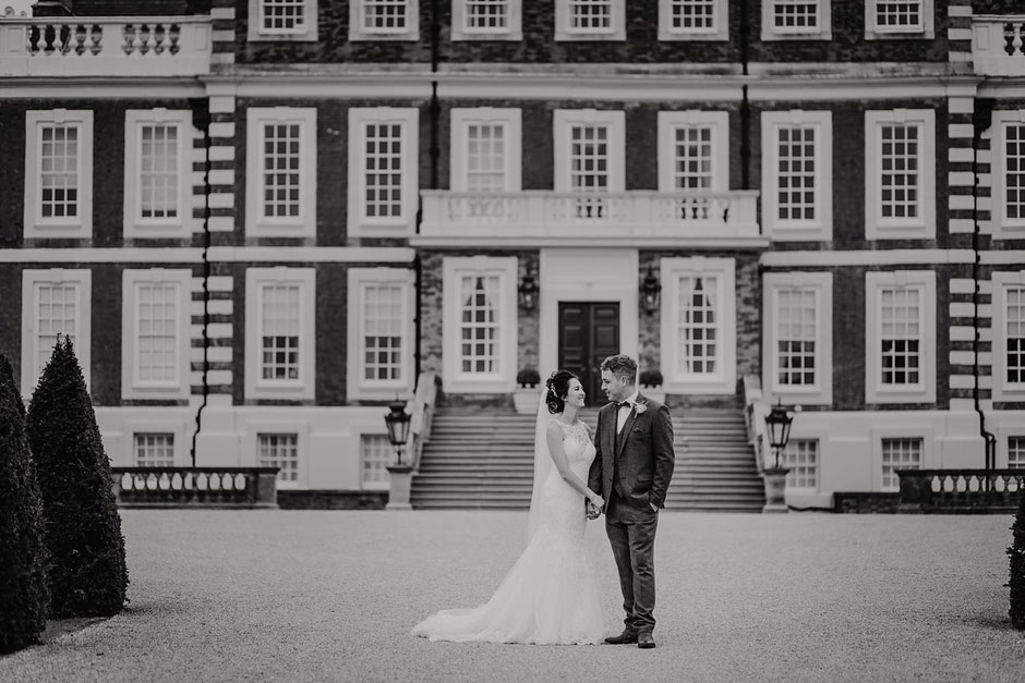 black and white portrait of a bride and groom smiling at each other in front of Knowsley hall