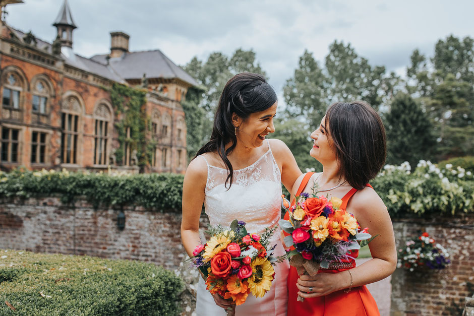 Bride and her bridesmaids looking at each other laughing. Holding colourful bouquets