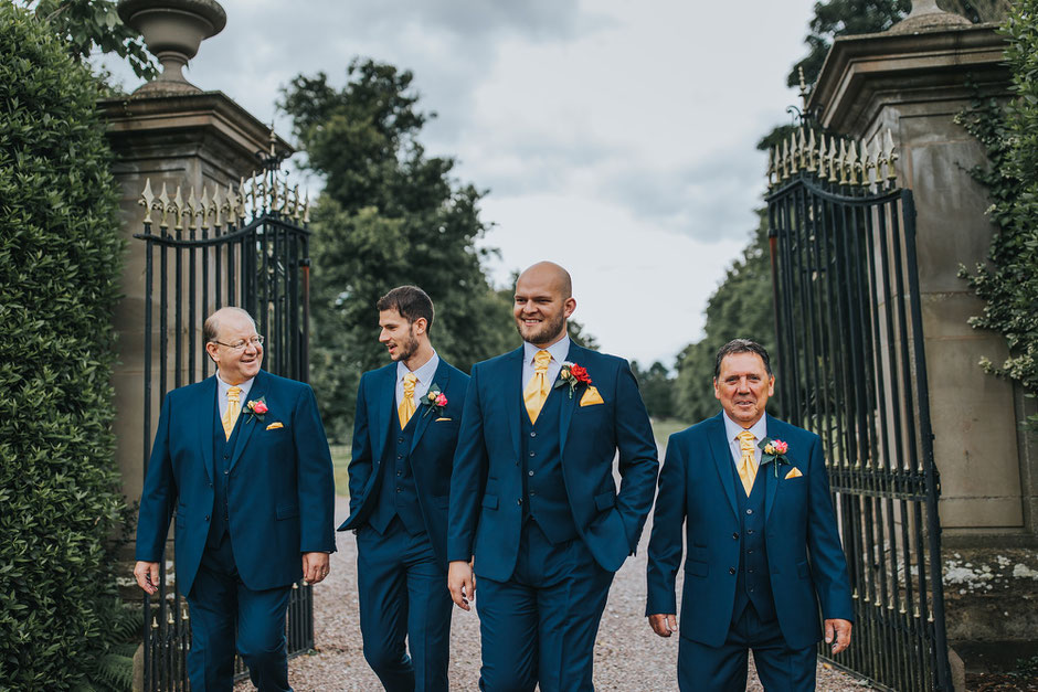 Groom and his grooms party dressed in Blue suits with yellow accents walking down the driveway at Soughton Hall