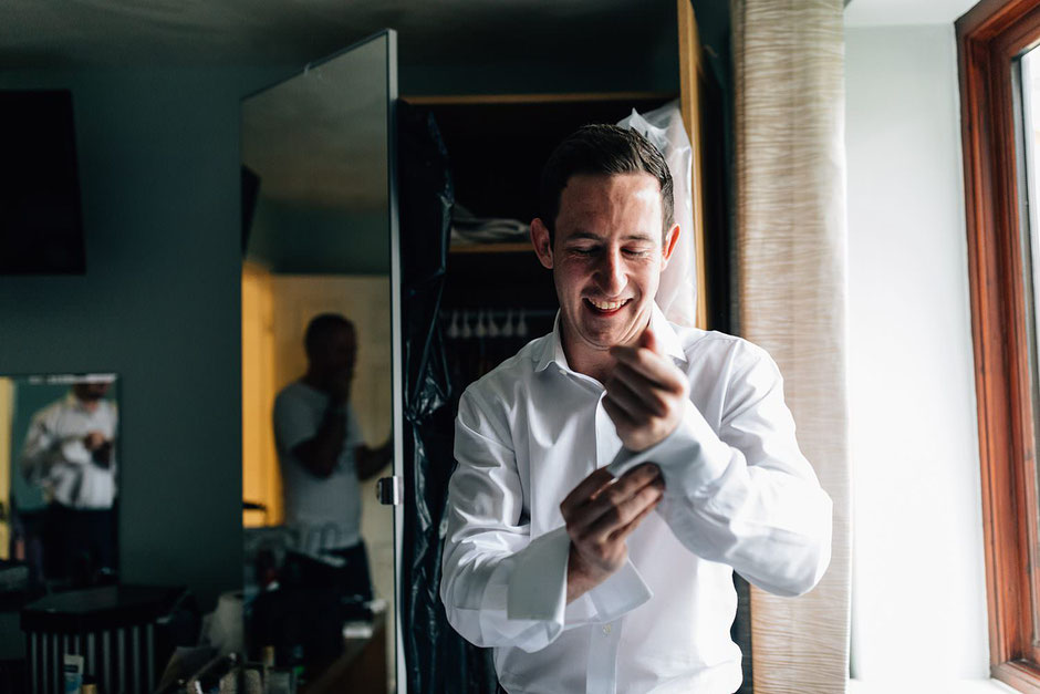 a photograph of a man fastening his shirt next to a window