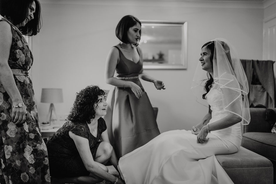 black and white photograph of a bride sat down whilst her Mum does her shoes up