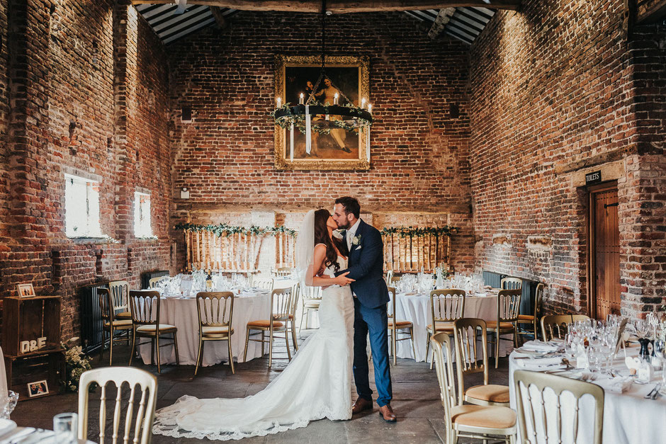 a bride and groom kissing in the barn at meols hall surrounded by their set up tables