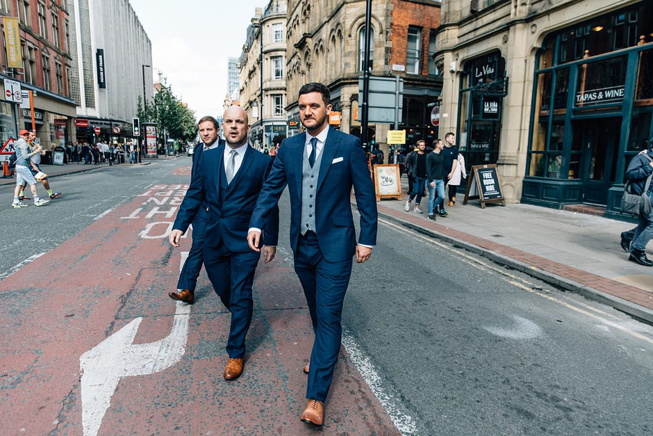 a groom and his best man walking to his wedding dressed in a blue suit in the city of manchester