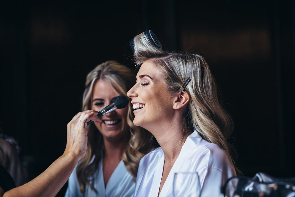 a bride having her make up done before her wedding and laughing
