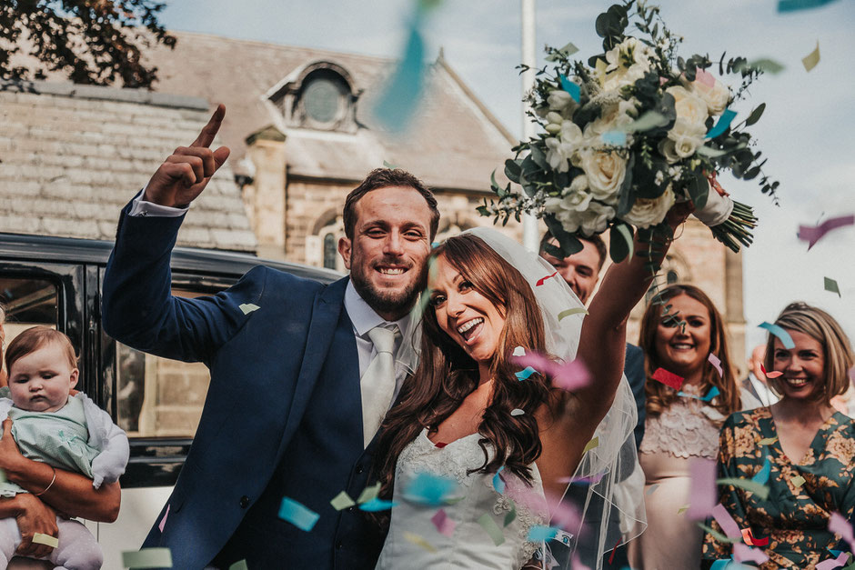bride and groom cheering outside church with confetti flying everywhere