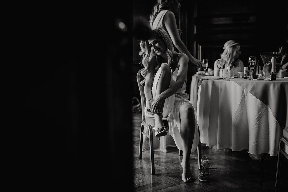 black and white photograph of a bride sat on a chair putting her shoes on