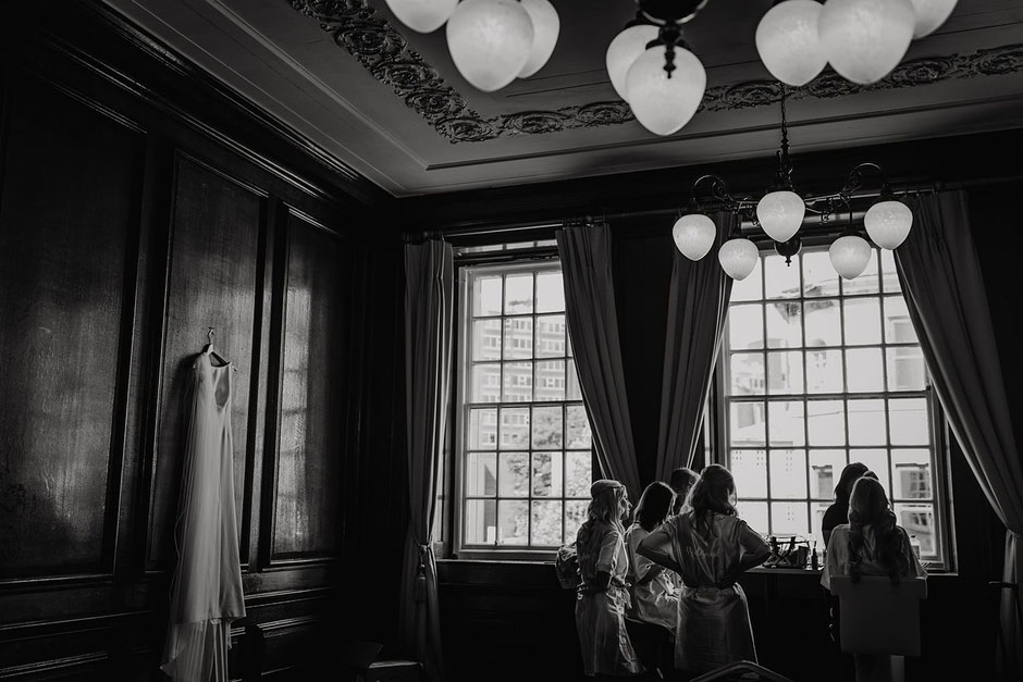 a wedding dress is hanging on the wall inside Manchester hall & a group of girls are stood around a table near a window