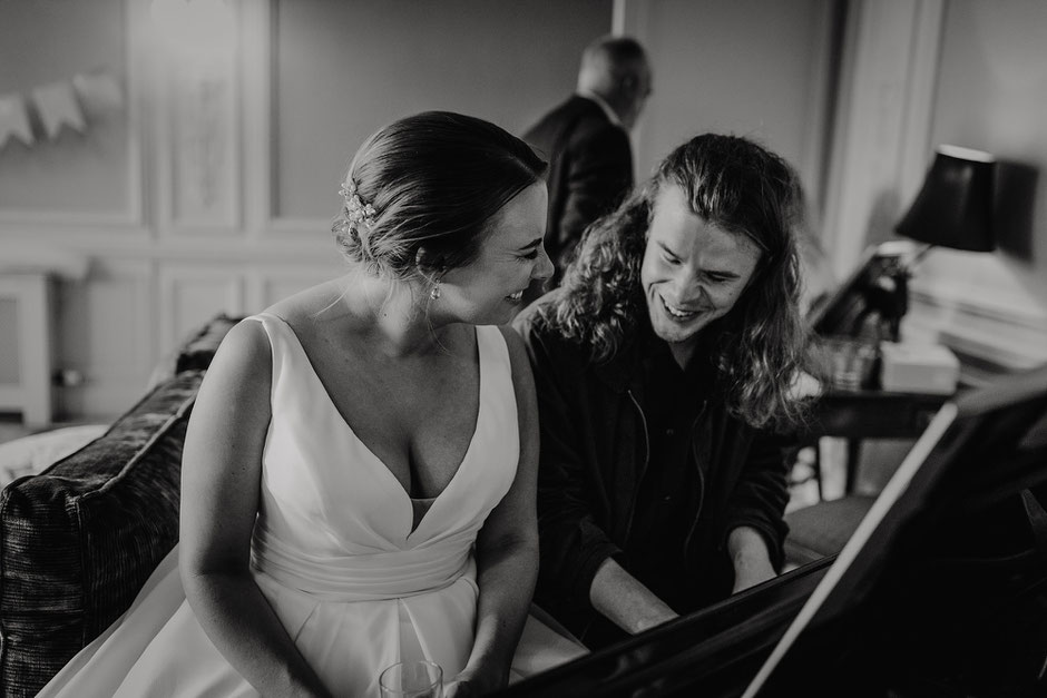 bride sat with her brother at a piano whilst he plays her a song
