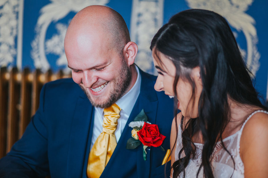 Bride and groom laughing as they sign the wedding certificate at Soghton Hall