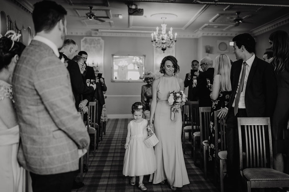 Bridesmaid crying and holding hands with a flower girl walking down the aisle