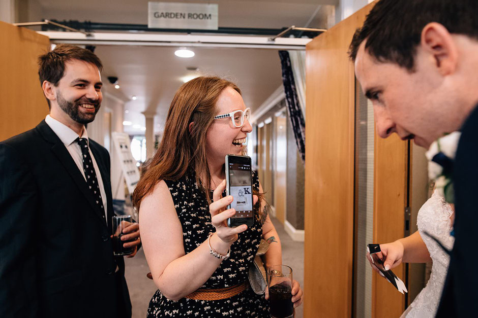 candid photograph of wedding guests laughing at a picture on a phone