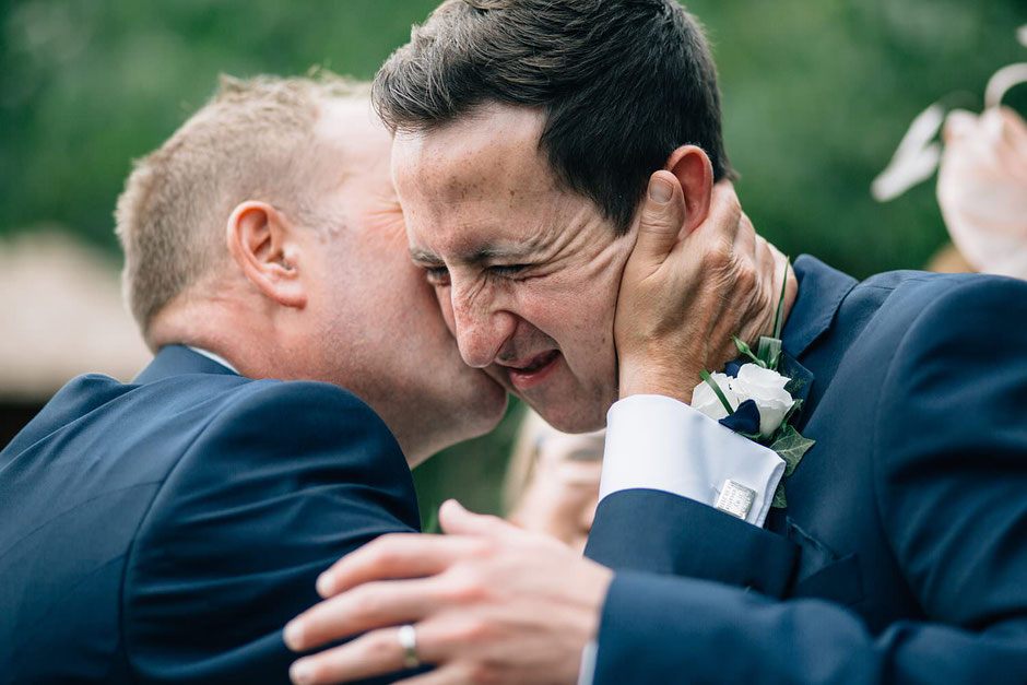 photograph of a groom being kissed my his new father in law and pulling a face