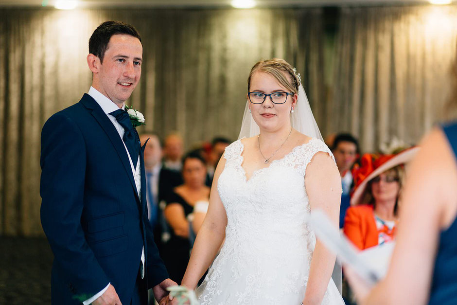 a bride and groom looking at the registrar marrying them