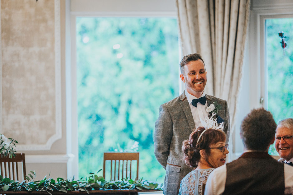 A candid photograph of a groom standing in the ceremony room waiting for his bride