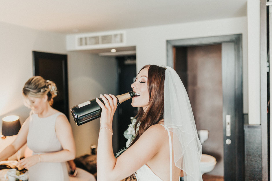 a bride in a veil drinking from a bottle of champagne