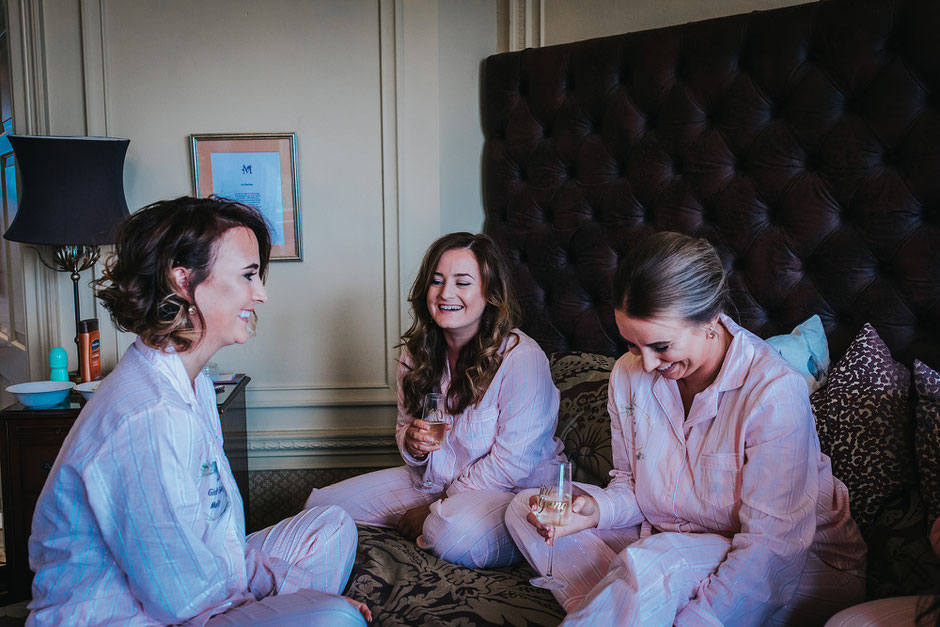 bridal party sat on a bed laughing with glasses of champagne all dressed in matching pyjamas