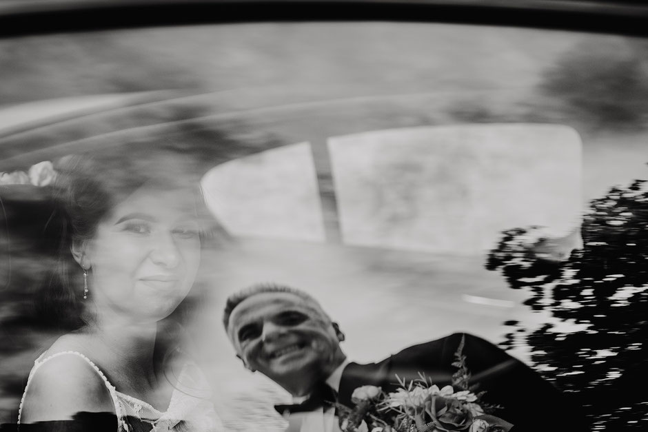 black and white photo of the bride sat in a car with her dads reflection on the window