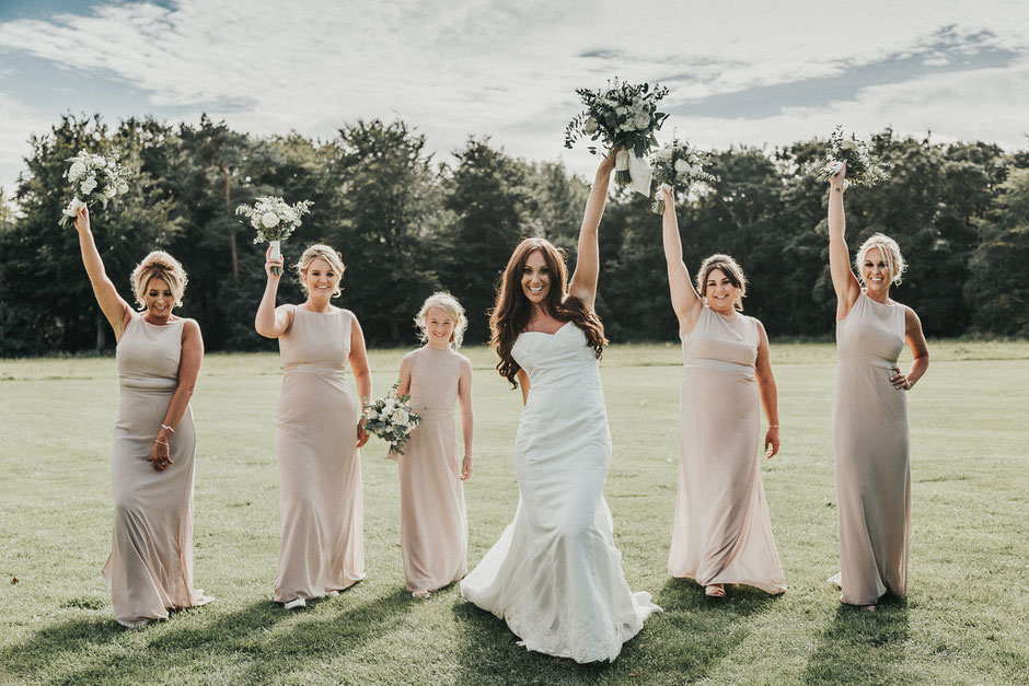 a bride and her bridesmaids walking toward the camera all holding their bouquets up in the air
