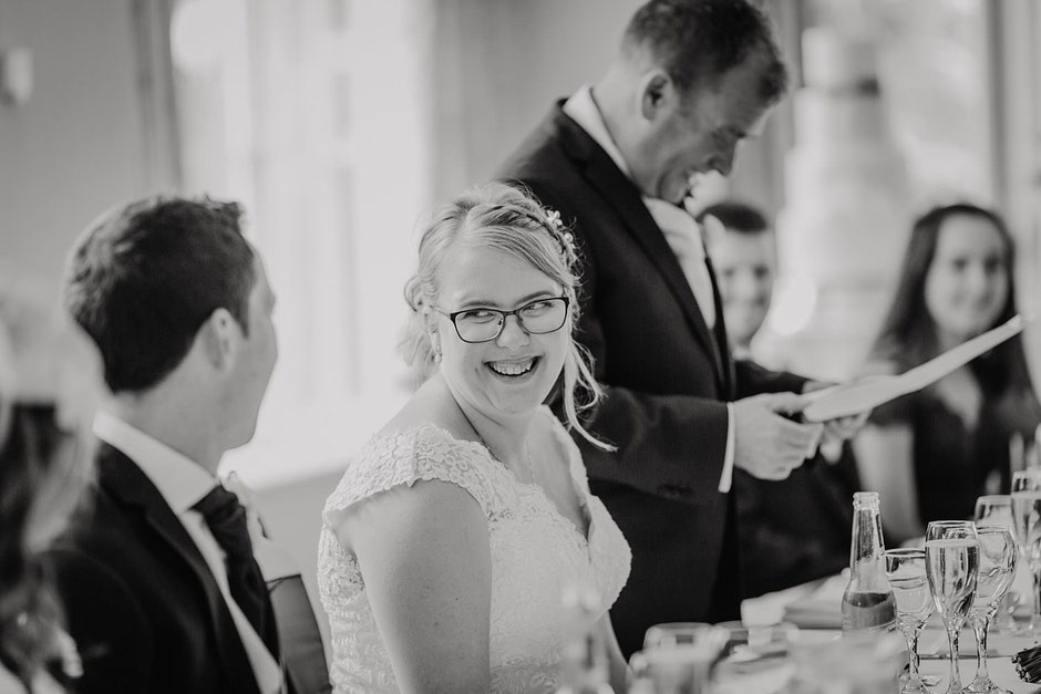 black and white image of a bride laughing towards the groom during speeches