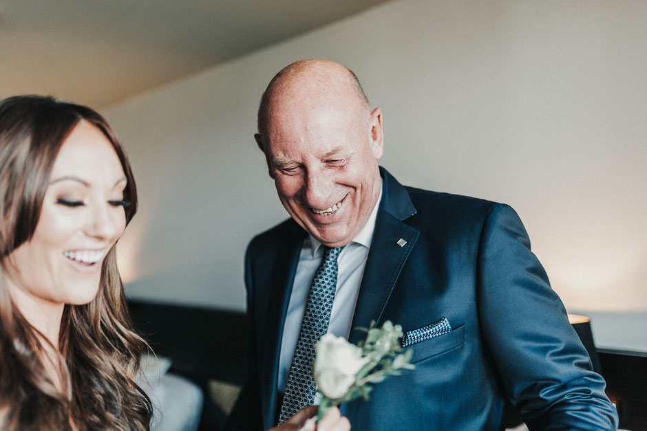 a bride helping her father attach his button hole to his suit