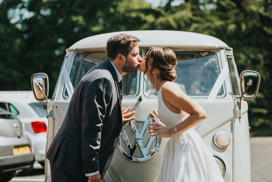 bride and groom kissing infant of their vw camper van