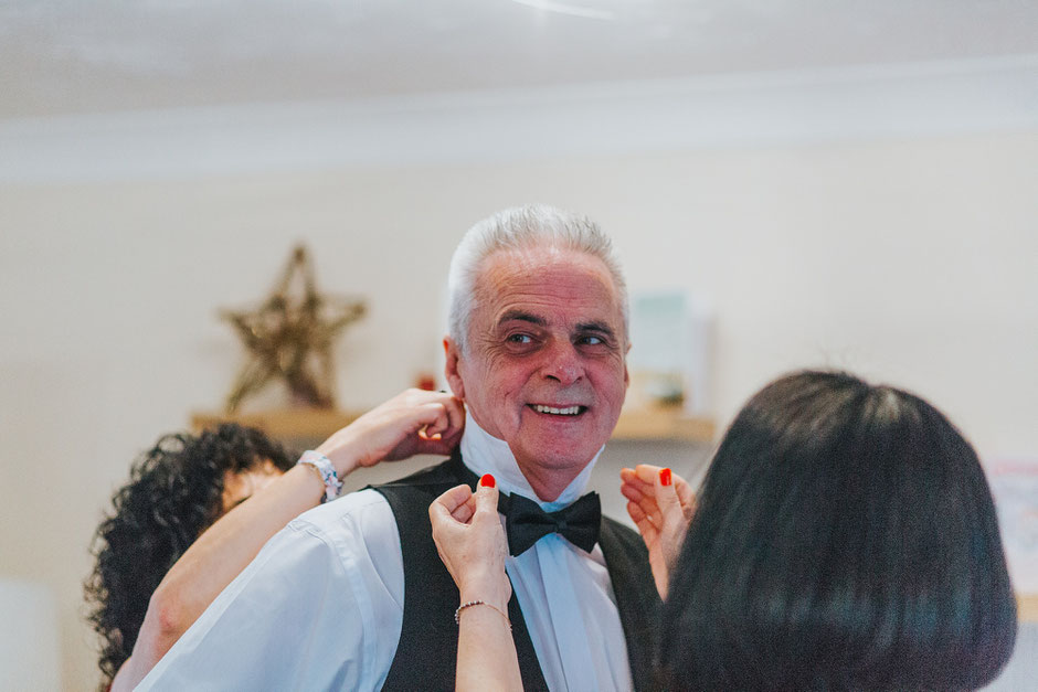 Father of the bride wearing a bowtie being dressed by two women