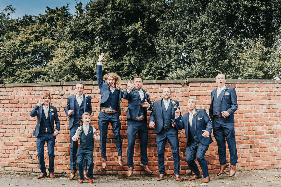 fun portrait of the grooms party all jumping in the air in blue suits and brown shoes