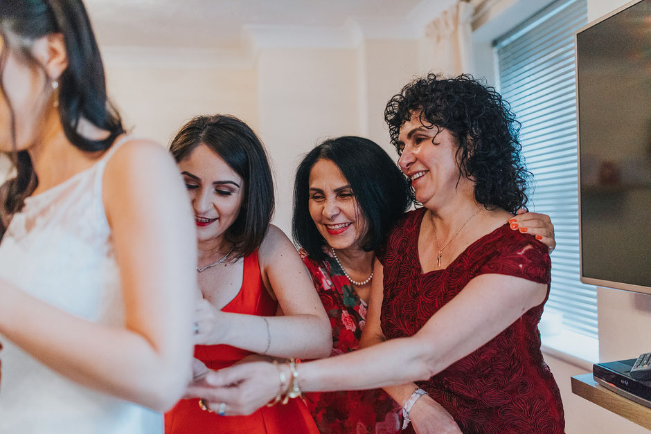three ladies all laughing whilst dressing a bride on her wedding day