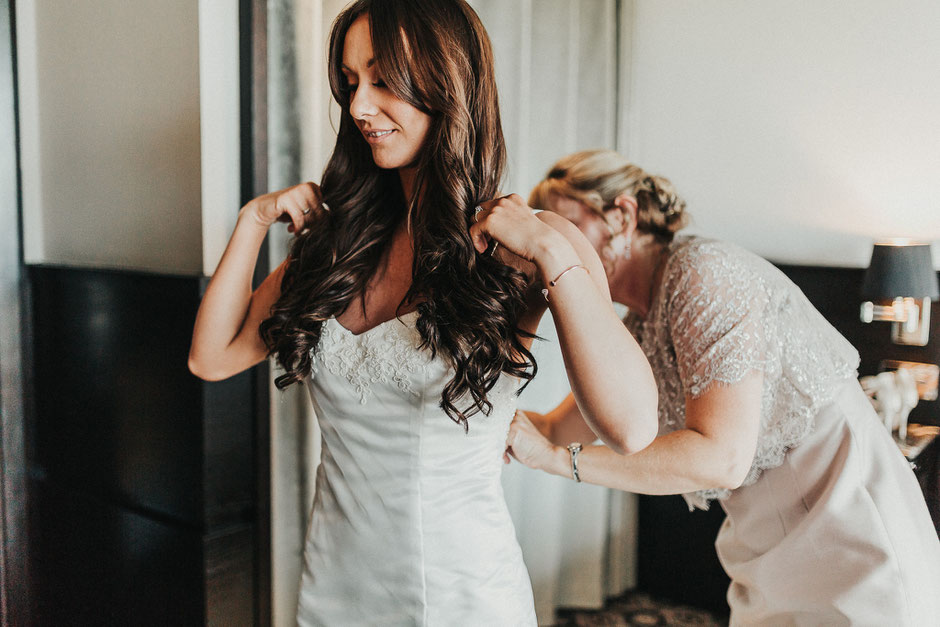 a bride in a hotel room being helped into her bespoke dress by her mum