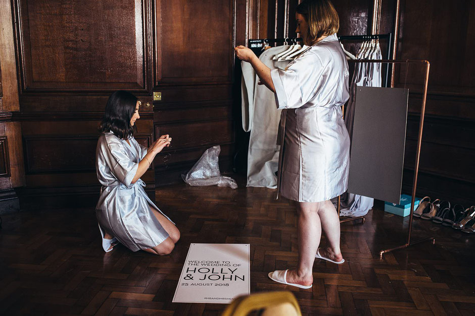 two bridesmaids dressed in silk robes hanging a wedding sign