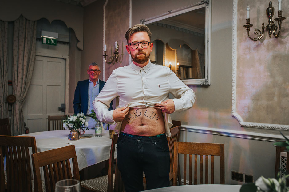 a man holding up his t shirt with the words thug life wrote on his belly