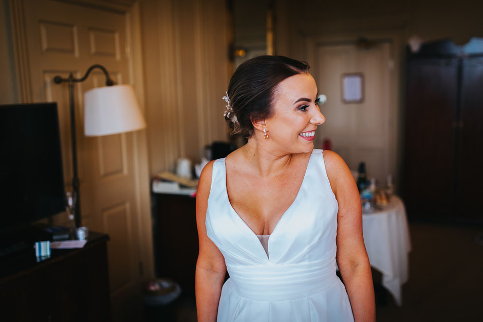 Bride looking towards someone at her side with a huge smiles on her face as she is getting dressed