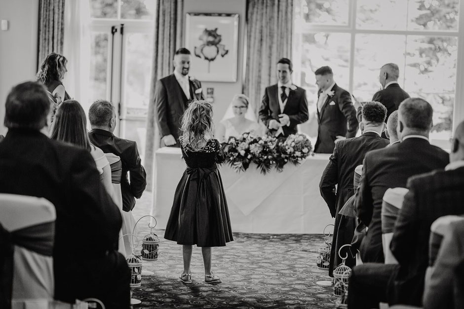 black and white photograph of a little girl taking a photo at a wedding