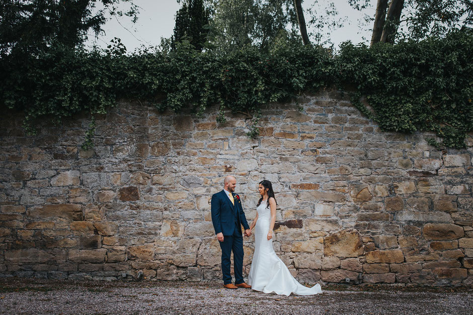 bride and groom holding hands in front of a large stone wall