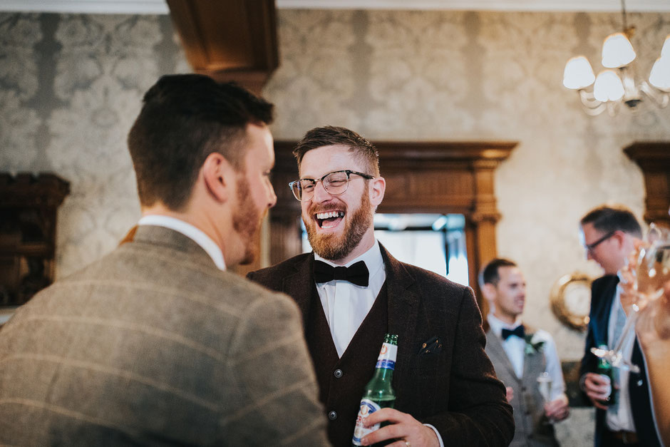 candid photo of a wedding guests wearing glassed and a bow tie laughing towards the groom