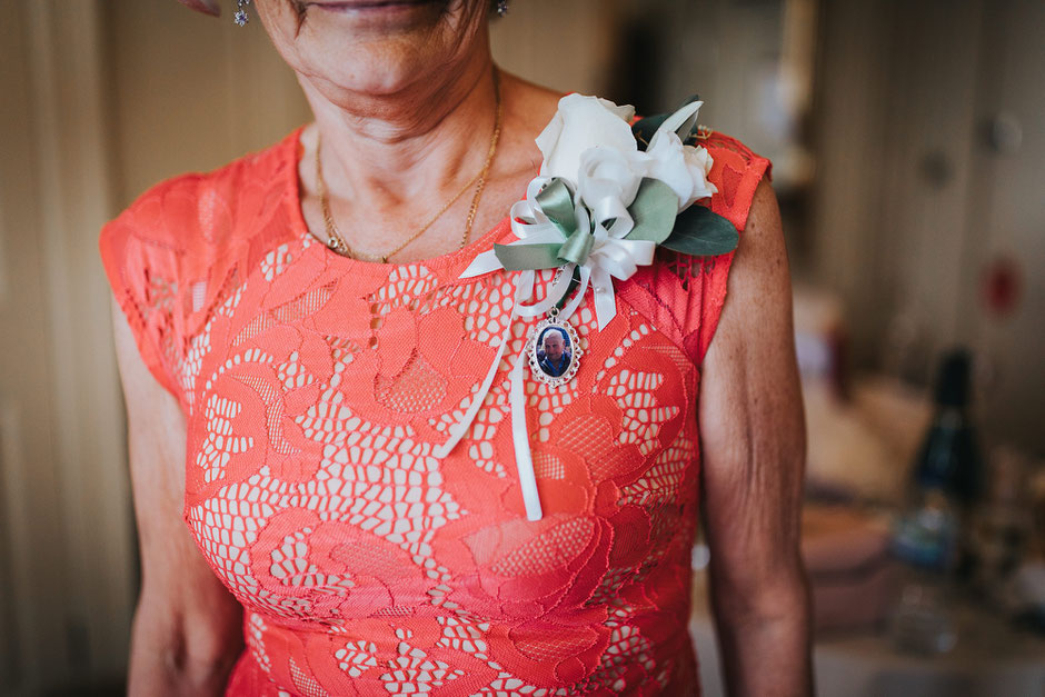 a memory charm brooch hanging off a ladies wedding day corsage