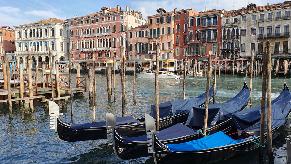 Der Canal Grande in Venedig mit im Wasser plätschernden Gondeln, im Hintergrund farbenfrohe Palazzi ©My own Travel