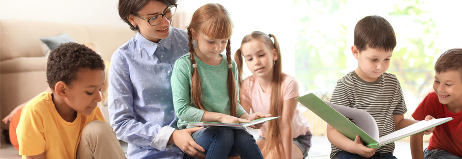 Symbolfoto: Eine Erzieherin sitzt mit Kindern in einer Runde und liest aus einem Buch vor