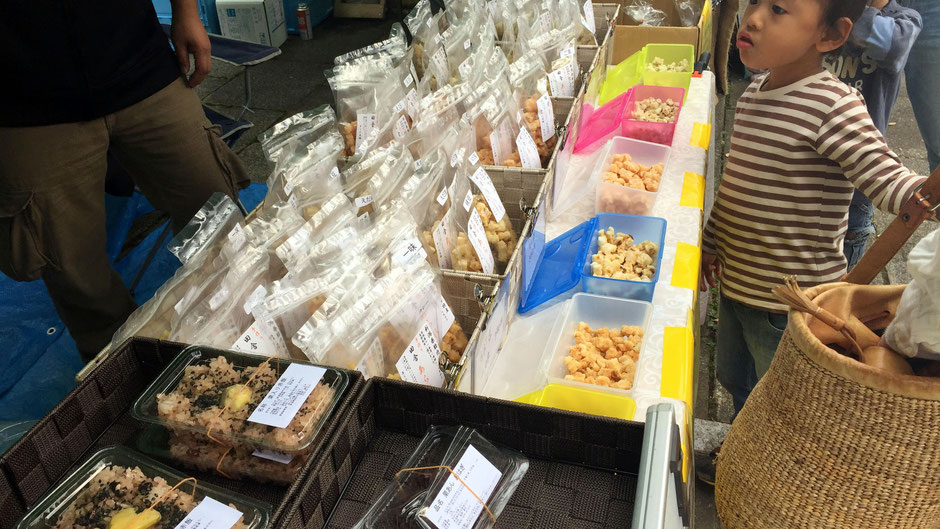 「Vege&Fork Market」(神奈川県川崎市麻生区)で出会った、あられ本舗おもやの、高橋重光さんです。たくさんの試食。お客さんに包囲され、接客で息つく暇もない。