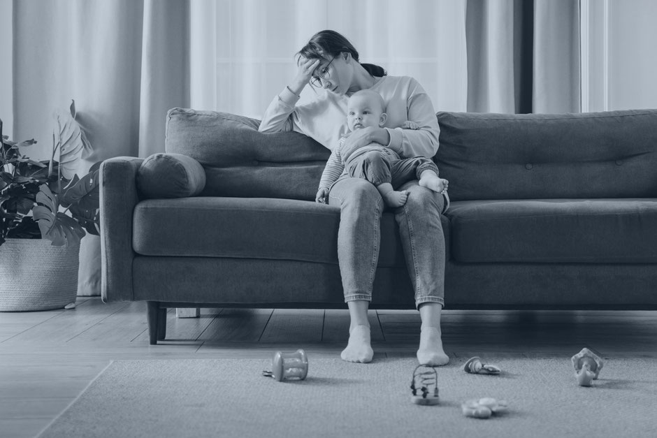 Frau mit Baby sitz auf dem Sofa und ist erschöpft