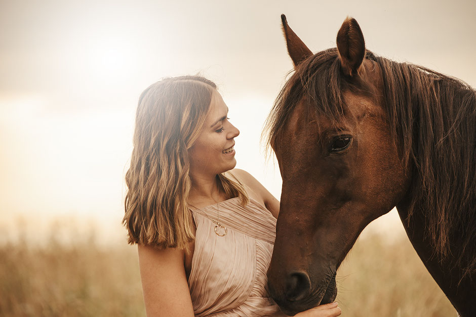 Frau mit Pferd im Sonnenaufgang auf der Weide