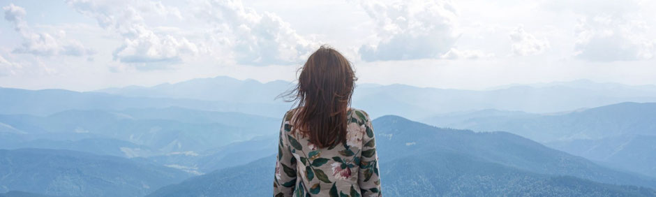Frau blickt in die Weite eines sanften Gebirgspanoramas und findet eine stille Perspektive auf ihr Leben.