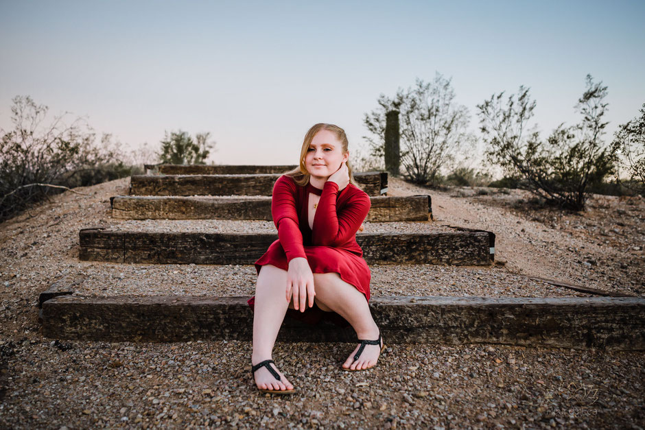 Senior girl in red dress sitting on wood natural steps. Fleur de Lea Photography